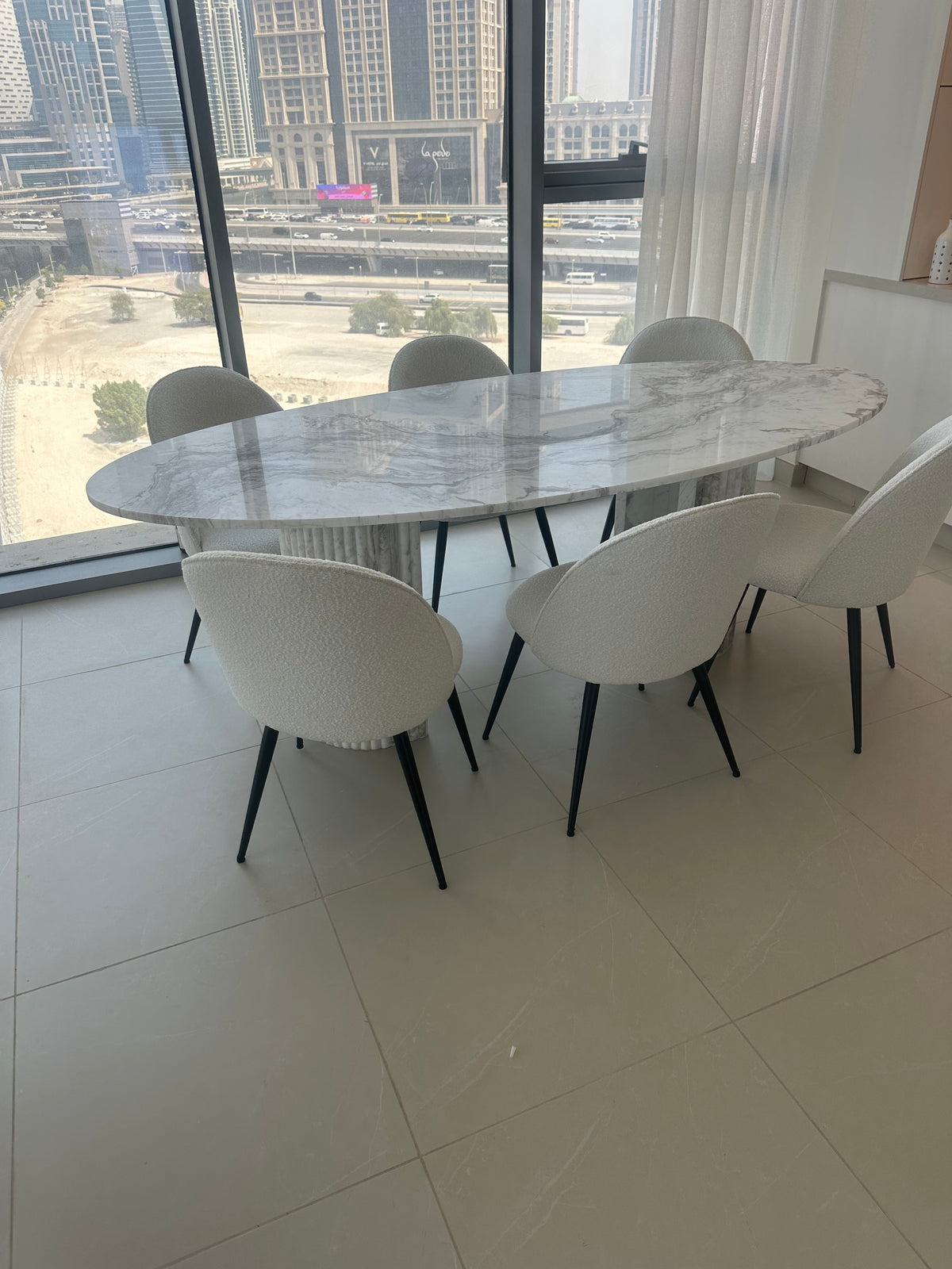 Volakas White Marble oval dining table with chairs in a Dubai apartment with city view